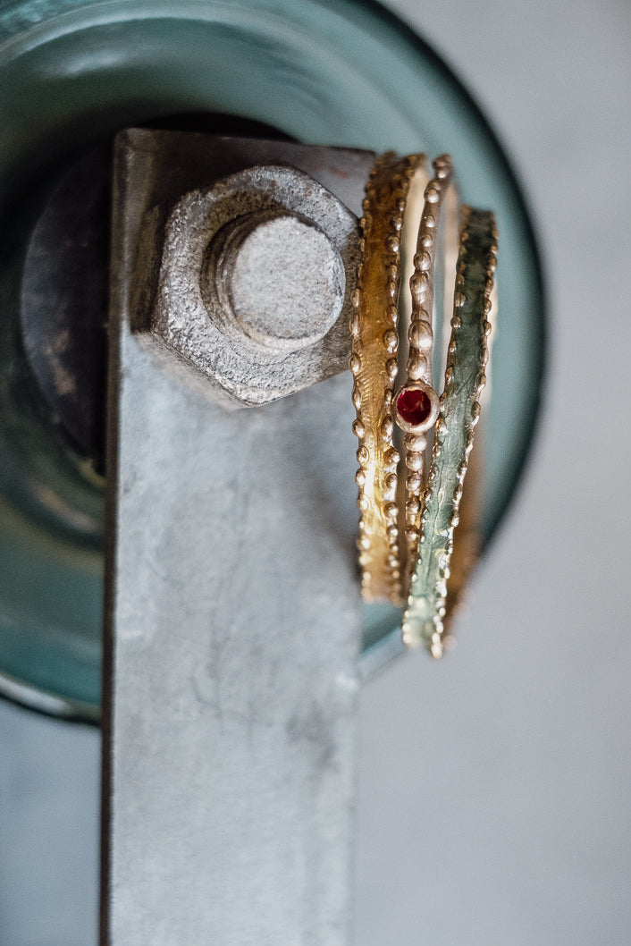 Three stacked bronze handmade bangles featuring a small red accent, displayed on a metal clamp.